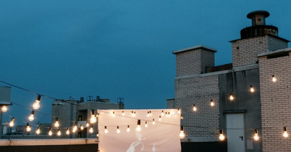 A group of friends enjoys a rooftop movie night under string lights with a projector and cozy blankets.