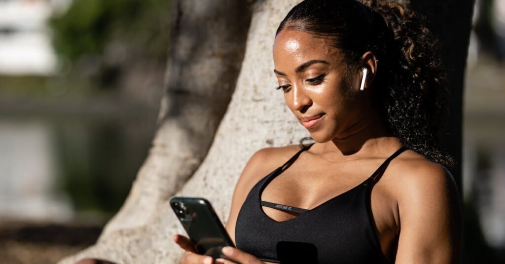 Woman in athletic attire using smartphone outdoors, enjoying a sunny day.