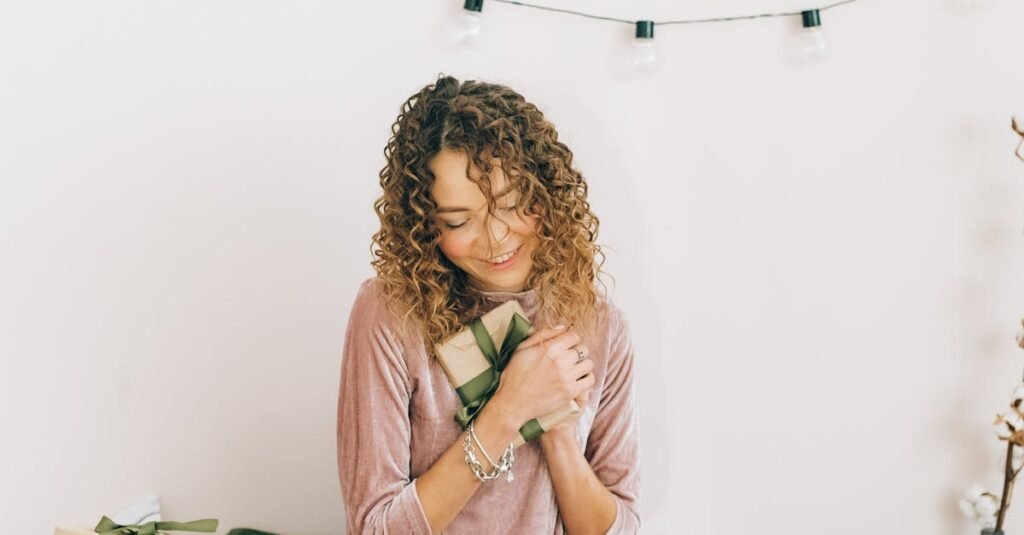 Smiling woman sitting with Christmas gifts and laptop, enjoying holiday moments indoors.